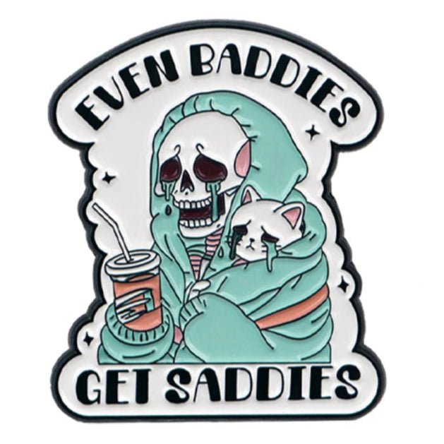 A cartoon skeleton in a teal hoodie and a sad white cat, both with tears and quirky cat pins. Bold text above and below says “EVEN BADDIES GET SADDIES.” By Kiss Me Later.
